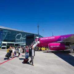 Pasażerowie wsiadają do różowego samolotu Wizz Air na płycie lotniska. Nowoczesny terminal lotniczy w tle.