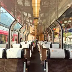 Wnętrze pociągu panoramicznego Bernina Express z wygodnymi siedzeniami i dużymi oknami, przez które widać góry.