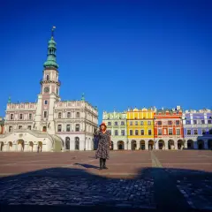 Kobieta w czerwonym kapeluszu na Rynku Wielkim w Zamościu, podziwiająca renesansową architekturę. Stare miasto w Zamościu zachwyca kolorowymi kamienicami.