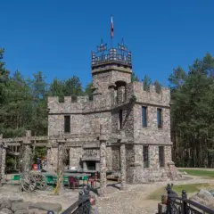 Kamienny zamek z wieżą i polską flagą, otoczony lasem. Nietypowe atrakcje Podlasia, które zaskakują.