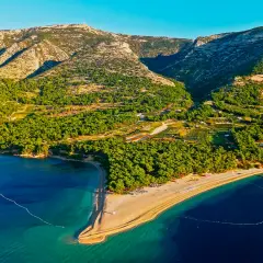 Idealne miejsce, gdzie na wakacje w lipcu: piaszczysta plaża otoczona zielenią, góry w tle i turkusowe morze.