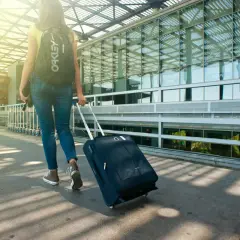 Kobieta z plecakiem i walizką na kółkach idzie w stronę lotniska. Pamiętaj o ubezpieczeniu samochodu na wyjazd do Chorwacji!