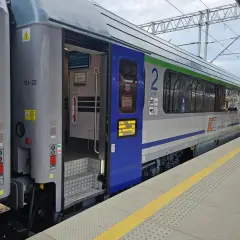 Eurocity train z otwartymi drzwiami na peronie. Widoczne schody, oznaczenia wagonu i fragmenty wnętrza.