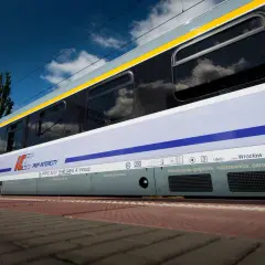 Pociąg Heweliusz PKP Intercity z Wrocławia, z widocznymi zbiornikami powietrza i klimatyzacją, na tle błękitnego nieba z chmurami.