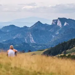 Para odpoczywa na trawiastym wzgórzu, podziwiając malownicze góry. To widok, który odpowiada na pytanie, gdzie leży Szczawnica.