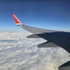 Skrzydło samolotu Norwegian nad chmurami. W tle błękitne niebo. Bagaż rejestrowany czeka na podróż.