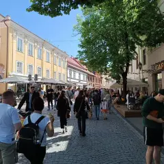 Tłum ludzi spaceruje po brukowanej ulicy w Wilnie, podziwiając architekturę i kawiarnie. Wygląda na to, że czy na Litwie jest bezpiecznie, bo atmosfera jest swobodna i radosna.