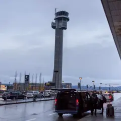 Wieża kontrolna na oslo lotnisko. Samochody i ludzie przy terminalu w deszczowy dzień.
