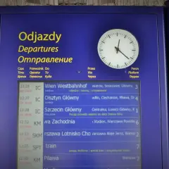 Tablica odjazdów PKP z zegarem. Widoczne pociągi do Wiednia, Olsztyna, Szczecina, Warszawy Zachodniej i innych. Kiedy zmiana rozkładu jazdy PKP, warto sprawdzić tablicę.