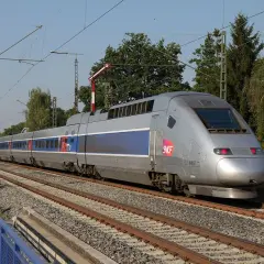 Srebrny pociąg TGV z niebieskimi pasami pędzi po torach, symbolizując niesamowitą prędkość.