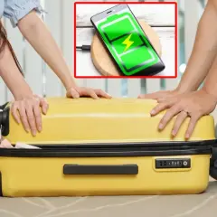 Para podróżnych zamyka żółtą walizkę. Telefon na ładowarce bezprzewodowej pokazuje pełną baterię, idealny na podróż z Wizzair, gdzie przyda się powerbank.
