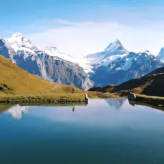 Osoba w czerwonej kurtce spaceruje nad jeziorem w Grindelwald, podziwiając ośnieżone szczyty Alp.