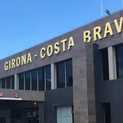 Złote litery "GIRONA - COSTA BRAVA" na nowoczesnym budynku lotniska.