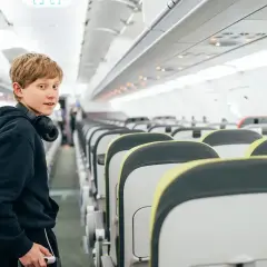 Chłopiec z słuchawkami na szyi w pustym samolocie. Zastanawia się, od ilu lat można latać samemu Ryanair.