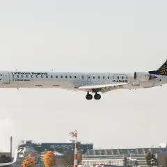 Samolot Lufthansa Regional z podwoziem wysuniętym do lądowania, leci nisko nad lotniskiem.