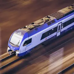 Nowoczesny pociąg Stadler FLIRT, z charakterystycznym niebiesko-białym malowaniem, pędzi po torach. To może być pociąg zamoyski, który zabiera pasażerów w podróż.