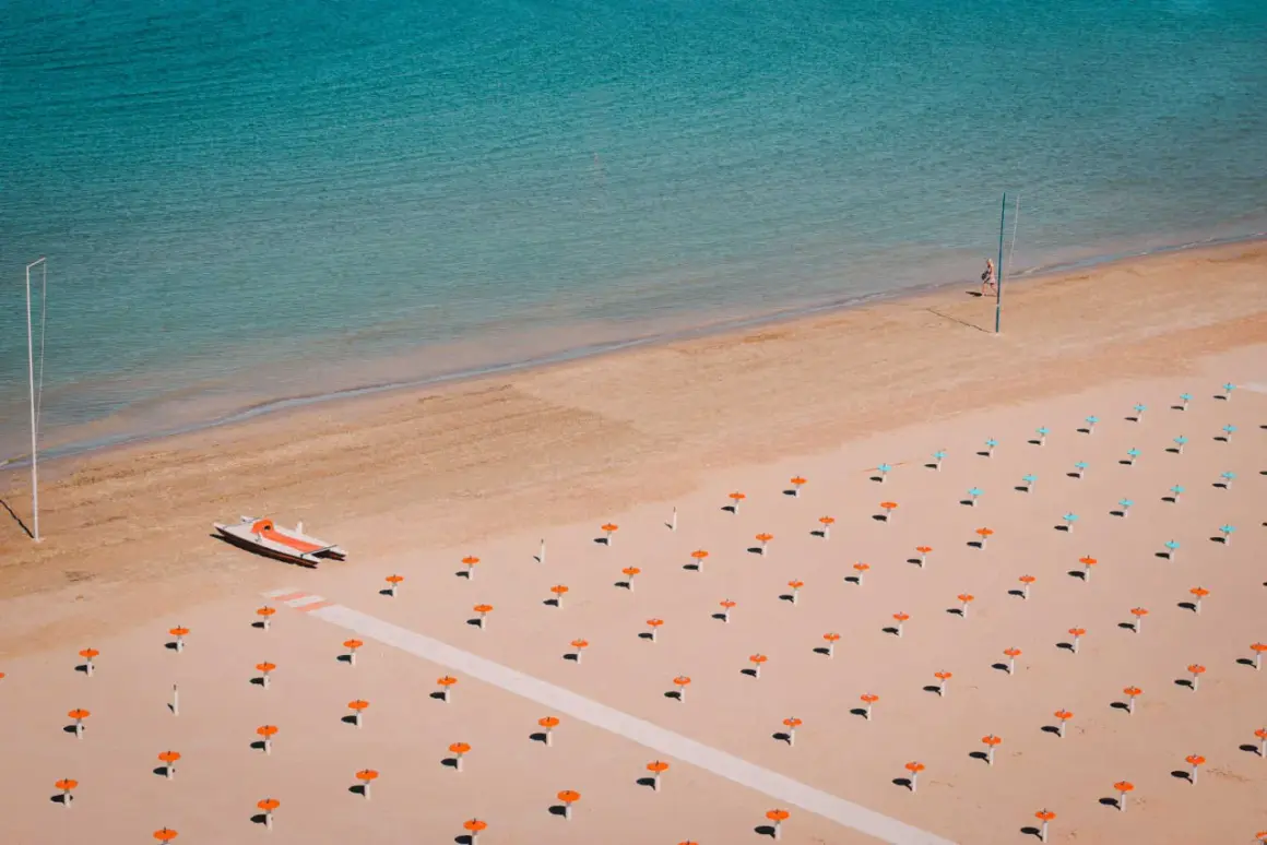 Pusta plaża w Rimini z rzędem parasoli i łodzią ratunkową.