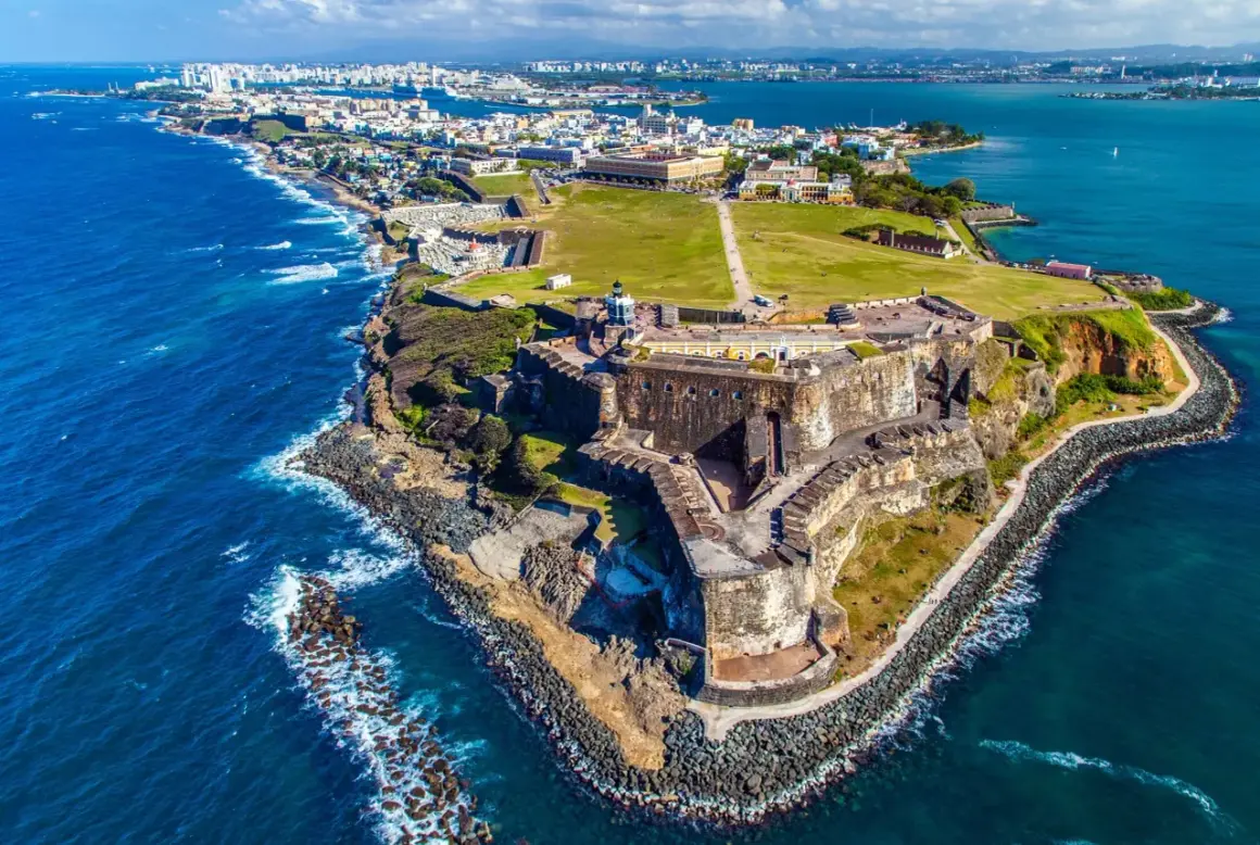 Widok na zabytkową fortecę i miasto San Juan, gdzie jest Puerto Rico. Błękitne morze otacza skaliste wybrzeże.