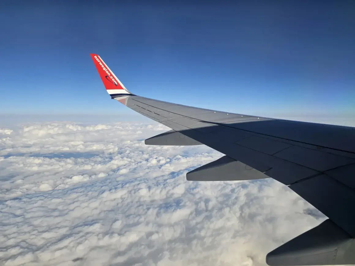 Skrzydło samolotu Norwegian nad chmurami. W tle błękitne niebo. Bagaż rejestrowany czeka na podróż.