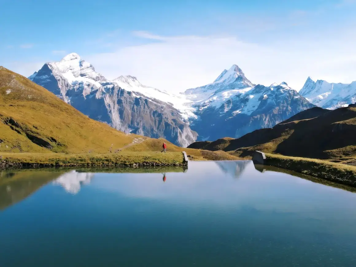 Osoba w czerwonej kurtce spaceruje nad jeziorem w Grindelwald, podziwiając ośnieżone szczyty Alp.