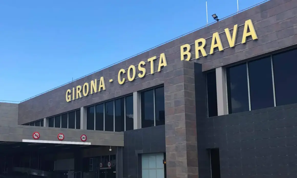 Złote litery "GIRONA - COSTA BRAVA" na nowoczesnym budynku lotniska.
