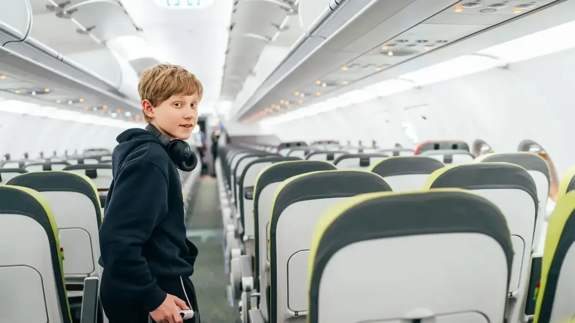 Chłopiec z słuchawkami na szyi w pustym samolocie. Zastanawia się, od ilu lat można latać samemu Ryanair.