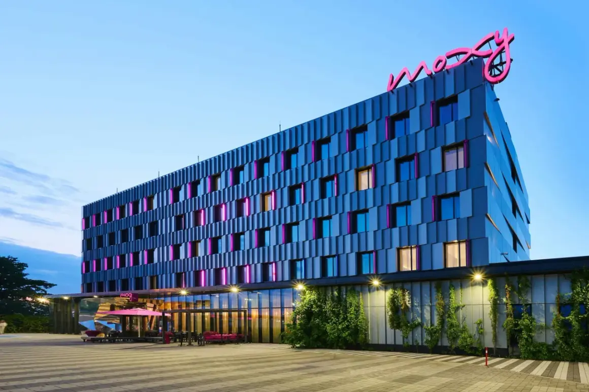 Nowoczesny hotel Moxy Hotels Pyrzowice z neonowym logo na dachu i kolorowymi podświetleniami okien.