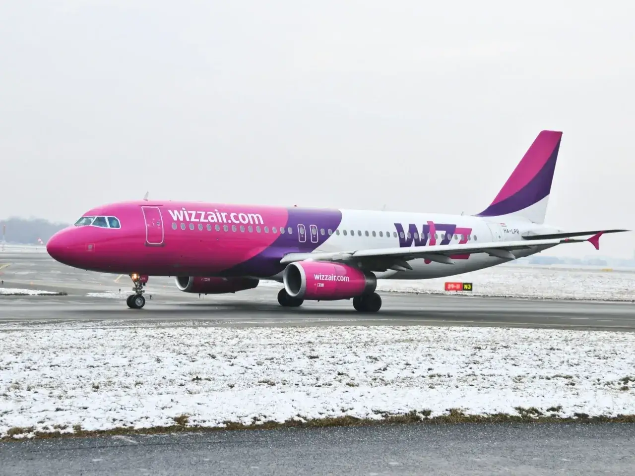 Różowy samolot Wizz Air na zaśnieżonym pasie startowym. Idealny moment na tanie loty w styczniu!