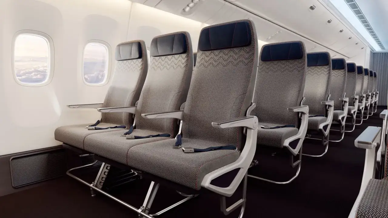Wizz rozkład miejsc w samolocie Wizzair. Rzędy szarych foteli z niebieskimi zagłówkami i pasami bezpieczeństwa, widok z okna na chmury.