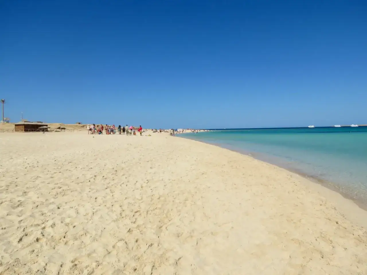 Plaża w Hurghadzie, gdzie leży ten raj. Piasek, turkusowa woda i łodzie na horyzoncie.