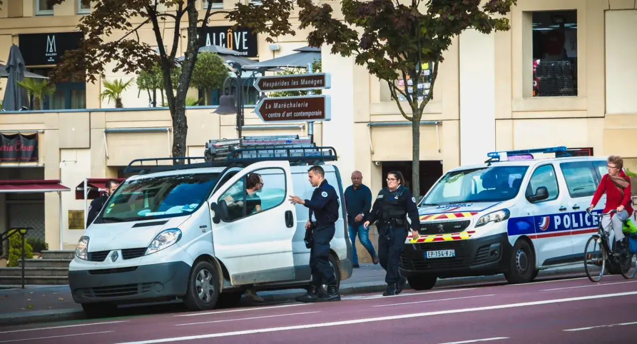 Francuscy policjanci przy radiowozach i furgonetce. Czy we Francji jest bezpiecznie? Widok ulicy z funkcjonariuszami i przechodniami.