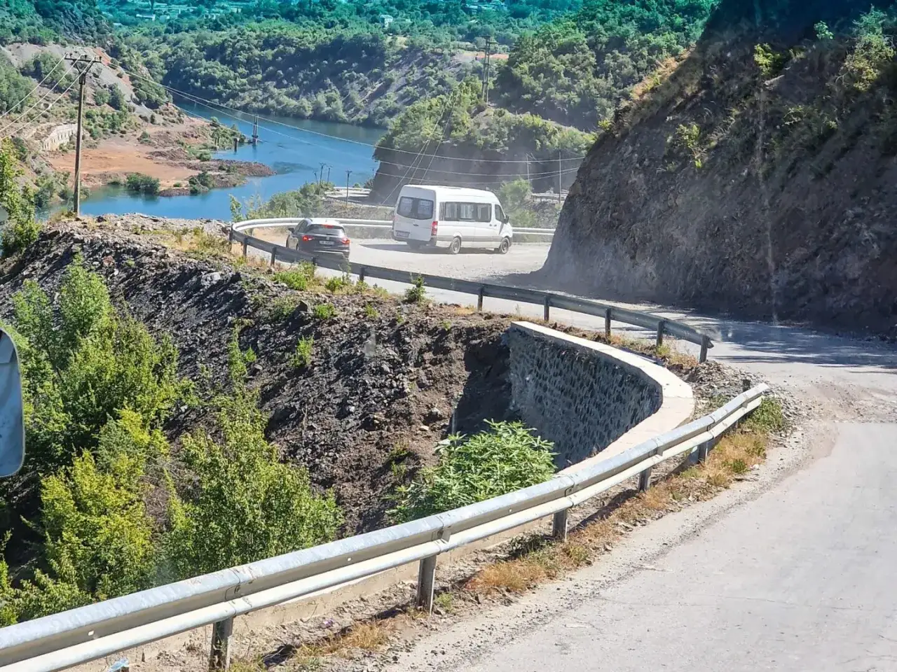 Kręta droga w Albanii, z samochodami i minibusem, prowadzi przez malownicze góry. Podróżni zastanawiają się, czy w Albanii jest bezpiecznie, ale widok zapiera dech w piersiach.