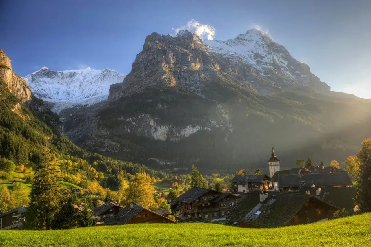 Malowniczy widok na Grindelwald, z ośnieżonymi szczytami gór, zielonymi łąkami i tradycyjnymi szwajcarskimi domami.