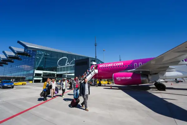 Pasażerowie wsiadają do różowego samolotu Wizz Air na płycie lotniska. Nowoczesny terminal lotniczy w tle.