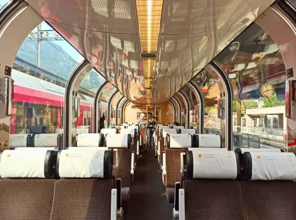 Wnętrze pociągu panoramicznego Bernina Express z wygodnymi siedzeniami i dużymi oknami, przez które widać góry.