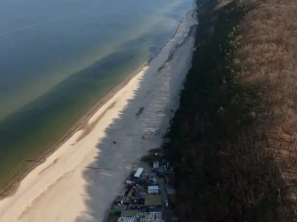 Plaża i las nad Bałtykiem. Połczyn-Zdrój odległość od morza jest niewielka, widać kilka domków i spacerowiczów.