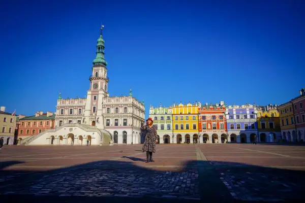 Kobieta w czerwonym kapeluszu na Rynku Wielkim w Zamościu, podziwiająca renesansową architekturę. Stare miasto w Zamościu zachwyca kolorowymi kamienicami.