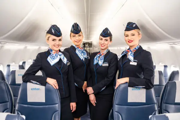 Uśmiechnięte stewardessy Enter Air w granatowych mundurkach i chustach z logo linii. Czy Enter Air jest bezpieczny? Tak, z taką załogą podróż będzie komfortowa.