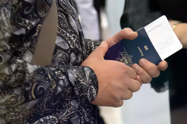 Ręce trzymają paszport i bilet lotniczy. Widoczne są dane do biletu lotniczego, takie jak numer lotu i bramka.