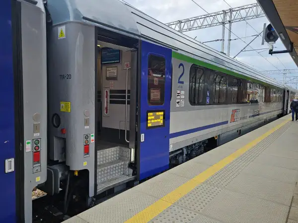 Eurocity train z otwartymi drzwiami na peronie. Widoczne schody, oznaczenia wagonu i fragmenty wnętrza.