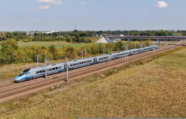 Nowoczesny pociąg Pendolino pędzi po magistrali kolejowej, mijając pola kukurydzy i zielone drzewa.