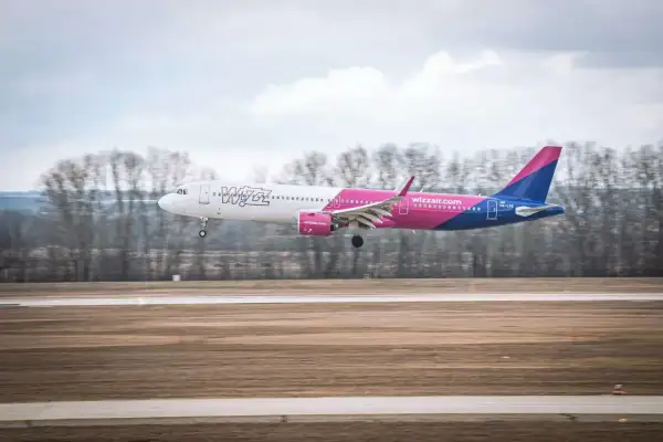 Samolot Wizz Air z różowym ogonem ląduje na pasie startowym. Wizz rozkład miejsc w samolocie Wizzair jest dobrze widoczny.