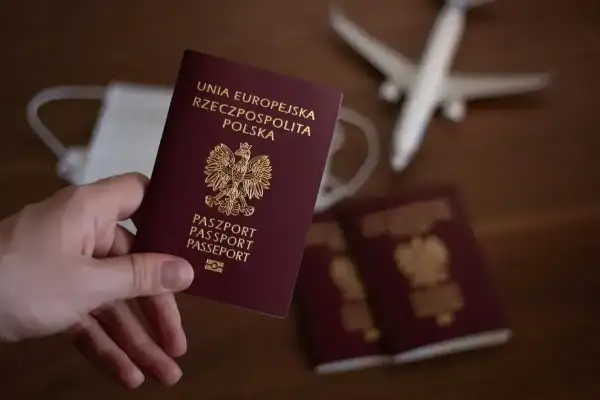 Dłoń trzyma polski paszport. Obok leżą inne dokumenty, maseczka i samolot. Zastanawiasz się, ile się czeka na paszport?