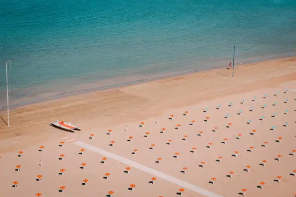 Pusta plaża w Rimini z rzędem parasoli i łodzią ratunkową.