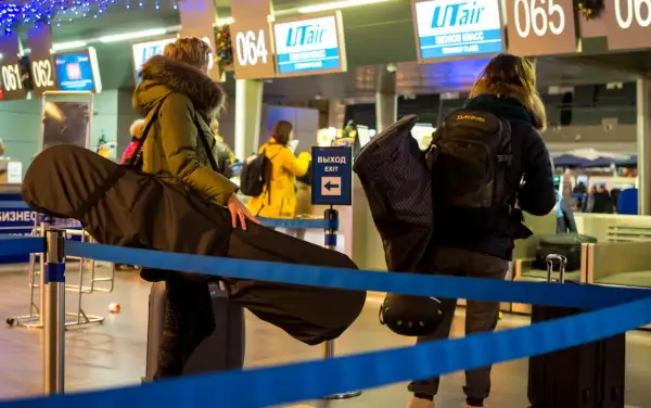 Osoby z bagażem sportowym, w tym futerałem na instrument, czekają na odprawę na lotnisku. Idealny bagaż sportowy Ryanair na podróż.