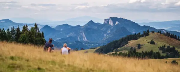 Para odpoczywa na trawiastym wzgórzu, podziwiając malownicze góry. To widok, który odpowiada na pytanie, gdzie leży Szczawnica.