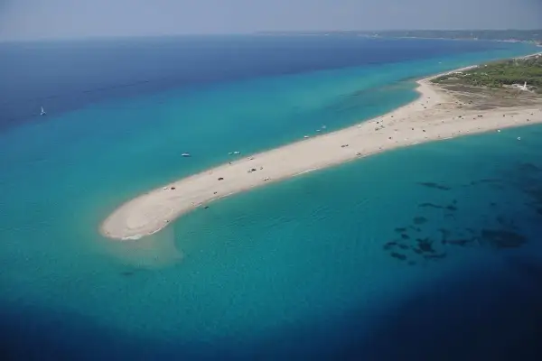 Piękna plaża na Chalkidiki, idealna na wakacje po przylocie na lotnisko. Woda turkusowa, piasek złoty, łodzie na morzu.