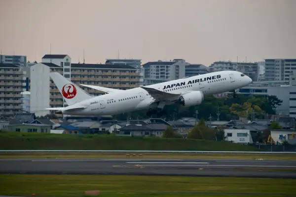 Samolot JAL Japan Airlines wznosi się nad miastem.