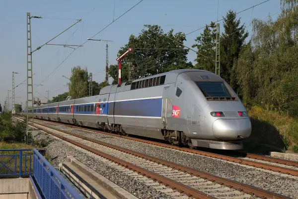 Srebrny pociąg TGV z niebieskimi pasami pędzi po torach, symbolizując niesamowitą prędkość.