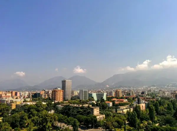 Widok na miasto z górami w tle. Widać nowoczesne budynki i zieleń. To ekuz Albania.